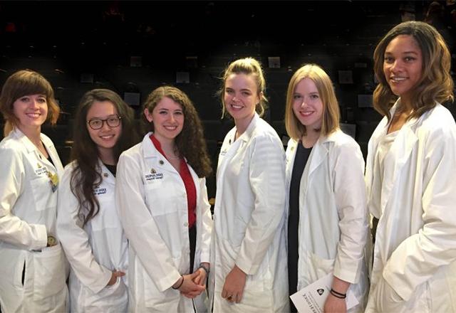 A group of female graduate students stand together with their white coats.